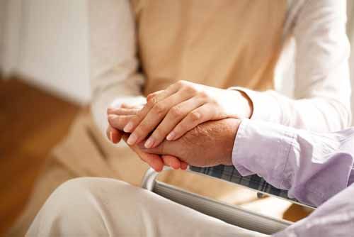 A personal care assistant holds an elderly man's hands